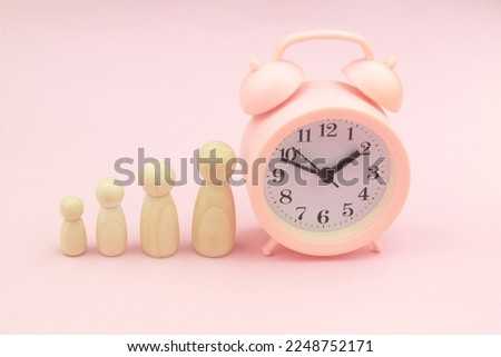 Different size female wooden figures and alarm clock on pink background. Growing up females and woman age concept.