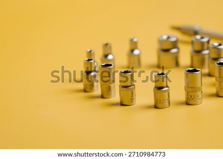 Different sizes of chrome sockets placed on a yellow surface with a pen nearby