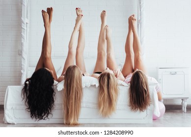 Different Skin Colors. Four Young Women With Good Body Shape Lying On The Bed With Their Legs Up.