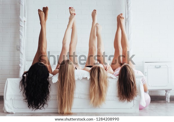Different skin colors. Four young\
women with good body shape lying on the bed with their legs\
up.