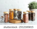 Different spices in glass jars on white marble table