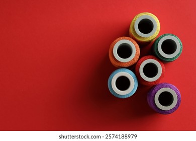 Different spools of sewing threads on red background, flat lay. Space for text