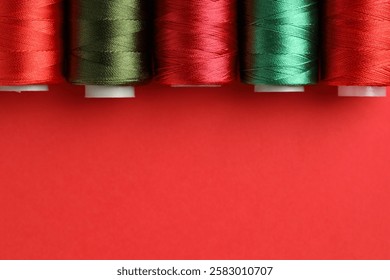 Different spools of sewing threads on red background, flat lay. Space for text