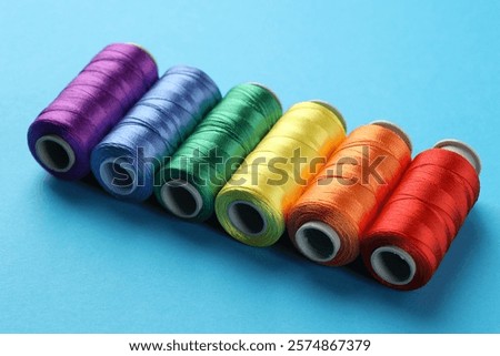Different spools of sewing threads on light blue background, closeup