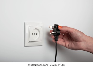 Different standards for electrical outlets. Unsuitable connector and plug in the hand of a person. Incompatibility, concept