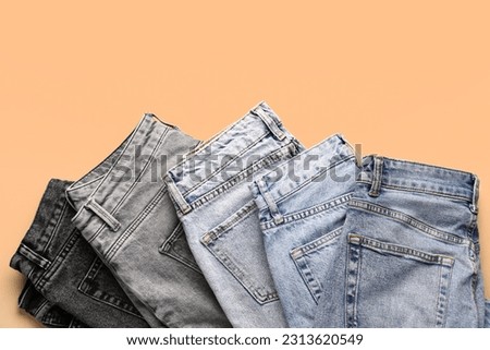 Different stylish folded jeans on pale orange background