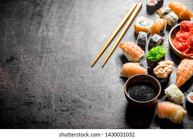 Different sushi with soy sauce and chopsticks. On dark rustic background