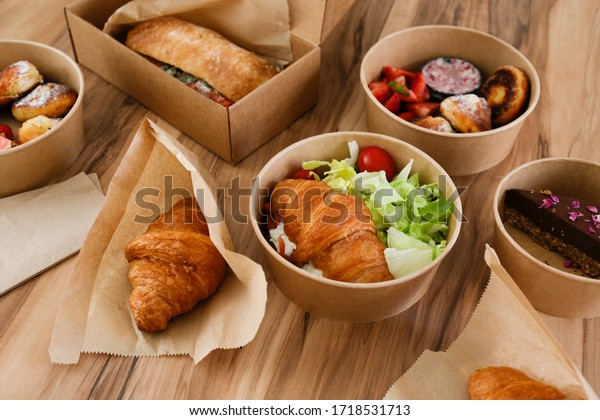 Different takeout food on wooden kitchen\
table. Italian panini sandwich, french croissant with salmon,\
strawberry pancakes and chocolate cheesecake. Close up, top view,\
pov, copy space,\
background.