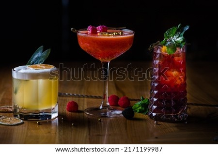 Different tasty cocktails on dark background. Beautiful line of three colorful alcoholic cocktails on a bar in a nightclub