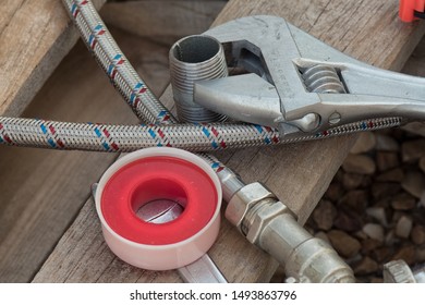 Different Things For Plumbers Lie On A Wooden Pallet. Teflon Tape, Wrench, Hose, Tube.