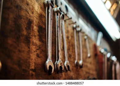 Different type of tools, especially wrenches, are hanging on the wall at workshop.