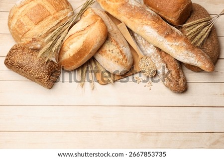 Different types of bread, grains and wheat spikes on wooden table, flat lay. Space for text