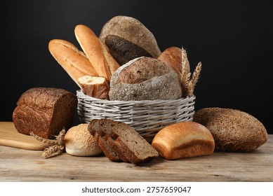 Different types of bread loaves and wheat spikes in wicker basket on wooden table against black background, closeup