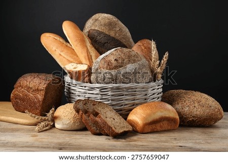 Different types of bread loaves and wheat spikes in wicker basket on wooden table against black background, closeup