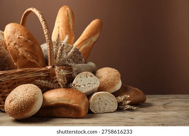 Different types of bread loaves in wicker basket on wooden table against brown background, closeup