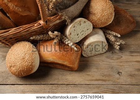 Different types of bread loaves in wicker basket on wooden table, closeup. Space for text