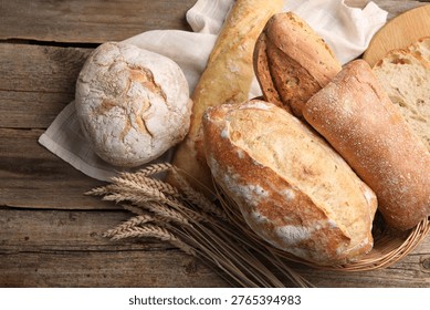Different types of bread and wheat spikes on wooden table, flat lay