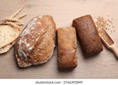 Different types of bread and wheat spikes on wooden table, flat lay