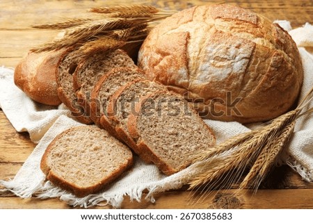 Different types of bread and wheat spikes on wooden table, closeup