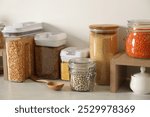 Different types of cereals and legumes in containers on light marble table in kitchen