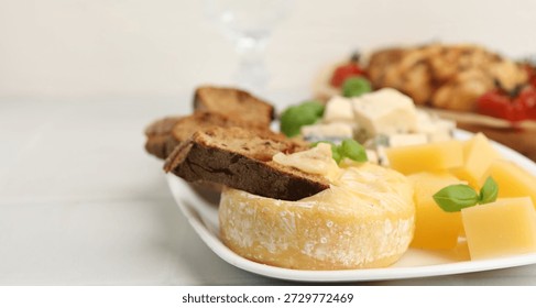 Different types of cheese, bread and basil on light tiled table, closeup. Space for text