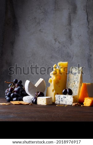 Different types of cheese. Cheeses mix maasdam, cheddar, dor blue, camembert, brie and grapes, walnuts, honey on wood table and dark grey background. 