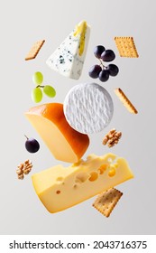 Different types of cheese are flying or falling in the air. Levitation concept. Cheeses mix or set maasdam, dor blue, camembert, brie and grapes, walnuts, galeta. Isolated. Copy space.