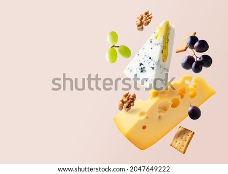 Different types of cheese are flying or falling in the air. Levitation concept. Cheeses mix maasdam, dor blue, camembert, brie and grapes, walnuts, galeta. Isolated. Copy space.