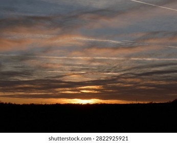Different types of clouds, golden sunlight and the peaceful nature captured in one picture. The colorful sky is decorated with clouds and strings pulled by air planes flying by. All creating a blissful atmosphere filled with peace and silence.
