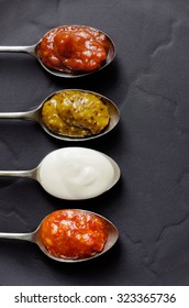 DIfferent Types Of Condiments On Vintage Spoons On Slate Background, Mayonnaise, Tomato Sauce, Mustard And Sweet Chilli Jam