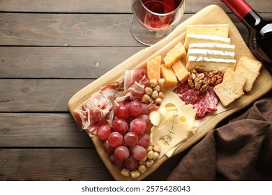 Different types of cut cheese and other snacks served with wine on wooden table, flat lay. Space for text