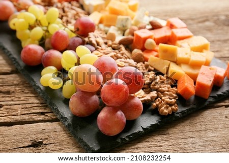 Different types of delicious cheese, nuts, grapes on a wooden background. Cheese platter: brie, camembert, blue cheese, emmental, parmesan, goat cheese, honey, grapes, walnuts, almonds. Healthy food. 