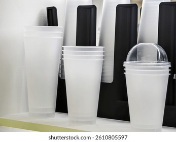 Different types of disposable cups, including clear and opaque styles, are organized on a shelf. The setting is casual, likely in a cafe, showcasing drinkware options.