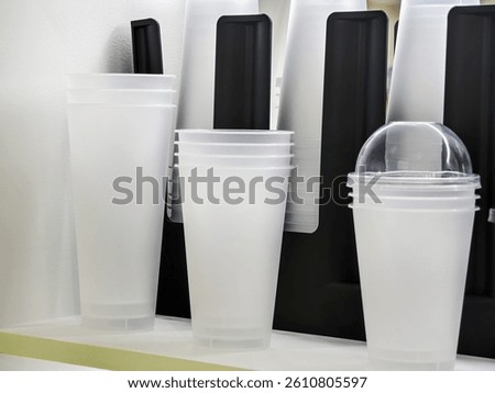 Different types of disposable cups, including clear and opaque styles, are organized on a shelf. The setting is casual, likely in a cafe, showcasing drinkware options.