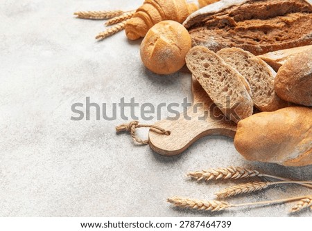 Different types of freshly baked bread and pastries on a wooden cutting board beside wheat ears