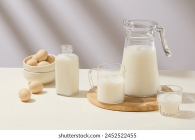 Different types of glass containers filled with fresh milk are arranged on white surface. A stack of ceramic bowls containing eggs. Tasty healthy dairy products on a table - Powered by Shutterstock