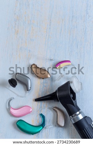 Different types of hearing aids are placed on a wooden surface. An otoscope is nearby, showing tools used for ear health and hearing assistance. This scene highlights audiology equipment.
