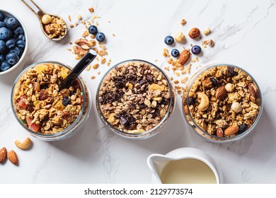 Different types of homemade granola (fruit, nut and chocolate) in jars on a white kitchen table, top view. Breakfast food concept. - Powered by Shutterstock