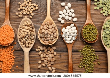 Different types of legumes in spoons on wooden table, flat lay