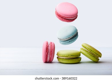 Different types of macaroons in motion falling on a white wooden background