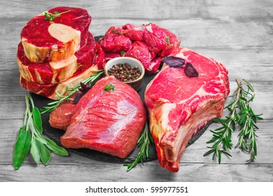 Different types of meat beef on round board. Herbs for an assortment of beef meat basil, thyme, rosemary, sage leaves, pepper. Light white wooden background.   
Top view from above and copy space. - Powered by Shutterstock