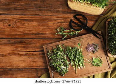 Different types of microgreens and scissors on wooden table, flat lay. Space for text