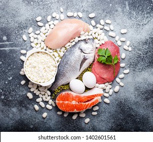 Different Types Of Natural Healthy Foods Contain Protein: Fish, Meat, Chicken, Eggs, Dairy Products, Beans On Gray Concrete Background, Top View, Closeup. Protein Foods For Diet And Proper Nutrition 
