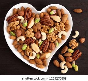 Different types of nuts on a plate in the shape of a heart. Top view.