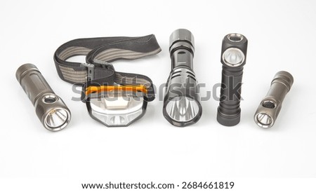 Different types of portable lights are placed together on a white surface, showcasing headlamps and handheld flashlights. Each light varies in design and intended use, illustrating versatility.