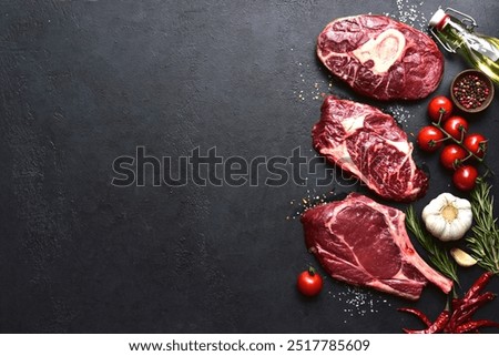 Different types of raw marbled beef steaks : T-bone, ossobuco, spider and rib eye with ingredients for cooking on a black slate, stone or concrete background. Top view with copy space.