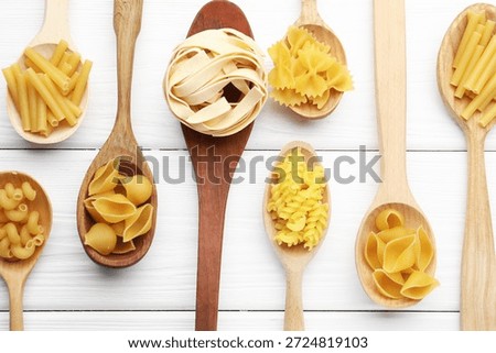 Different types of raw pasta in spoons on white wooden table, flat lay