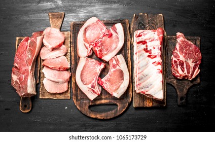 Different types of raw pork meat and beef. On the black chalkboard.