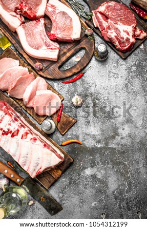 Different types of raw pork meat and beef with spices and herbs. On rustic background.