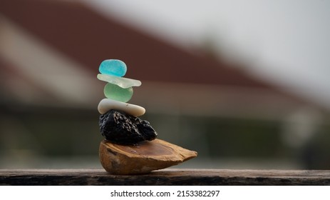 Different types of stone pebbles including sea glass and lava stone balancing on a plain rock
